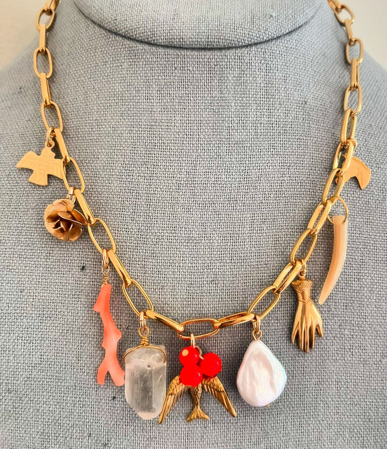 Gold necklace with various charms on a gray mannequin